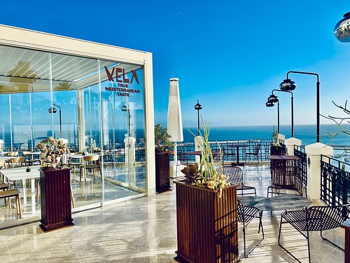 Terrazza di Vela Ristorante a Sciacca con vista sul porto e sul mare, area esterna luminosa e sala vetrata.