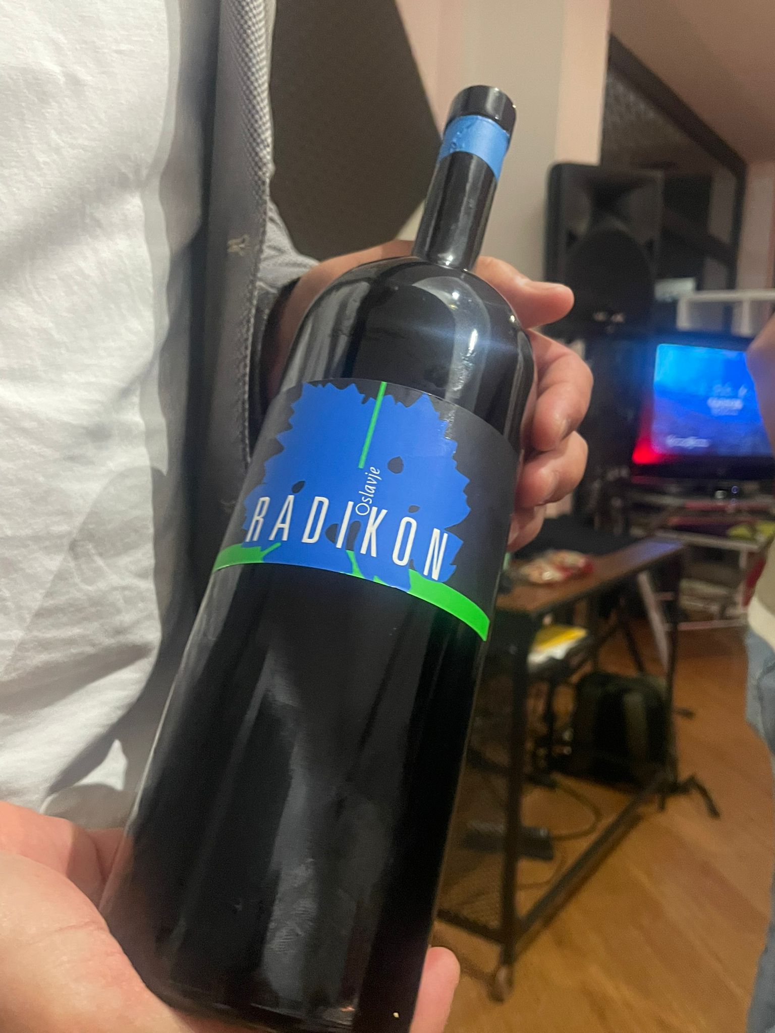 Bottiglia di vino Radikon Oslavje con etichetta blu caratteristica tenuta in mano da una persona con camicia bianca, tappo con capsula blu